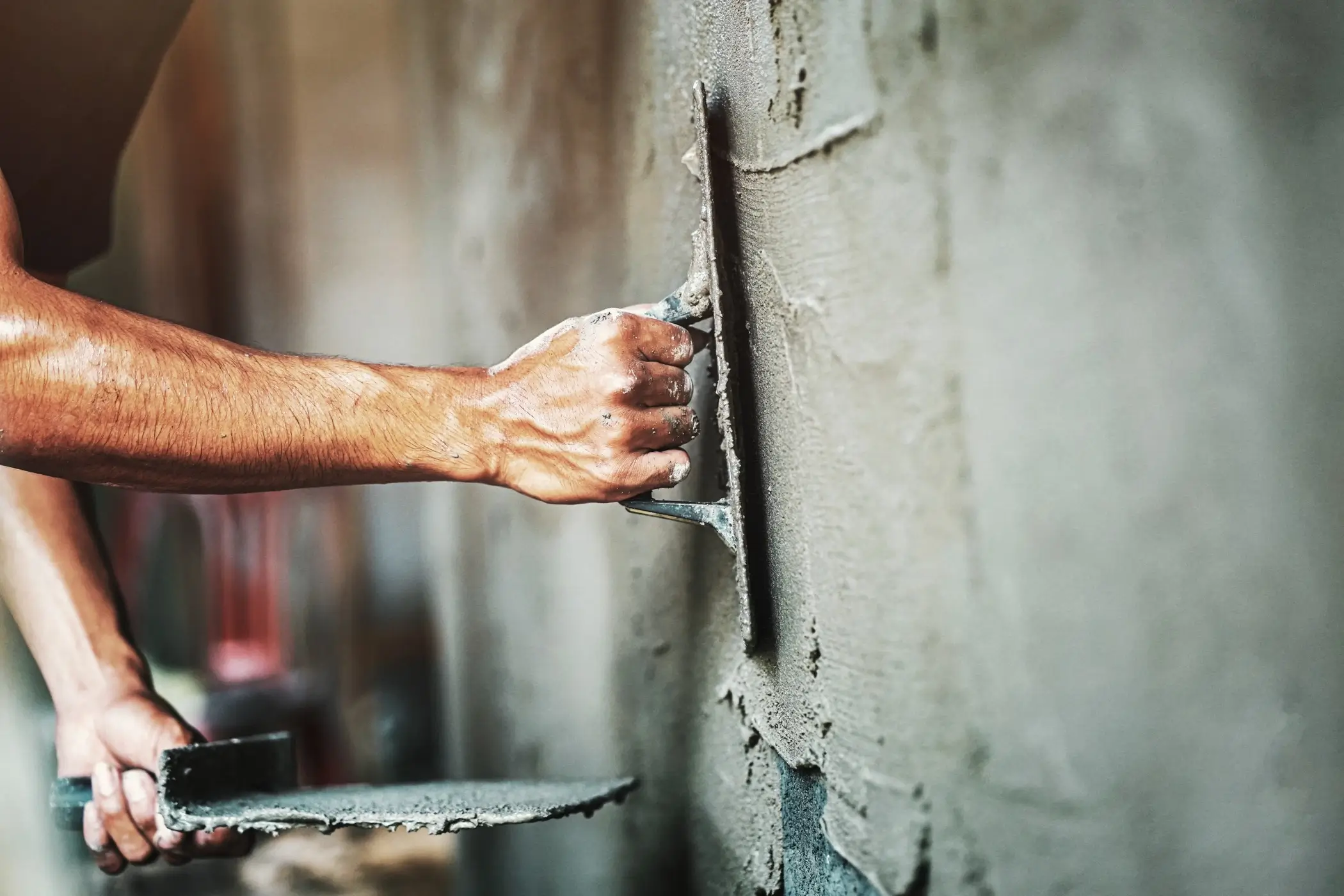 Maçon appliquant du plâtre sur un mur avec une truelle pour une finition lisse.