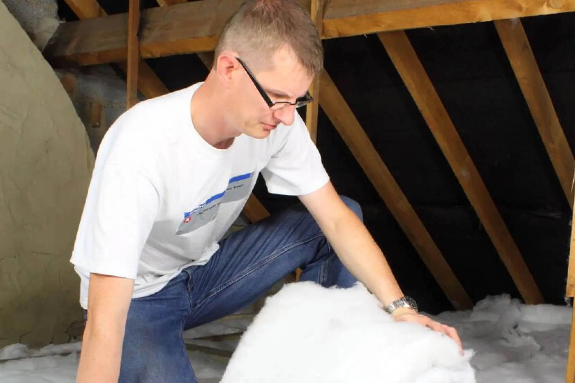 Installateur en vêtements de travail posant des rouleaux d'isolation en fibre de verre sur un plancher