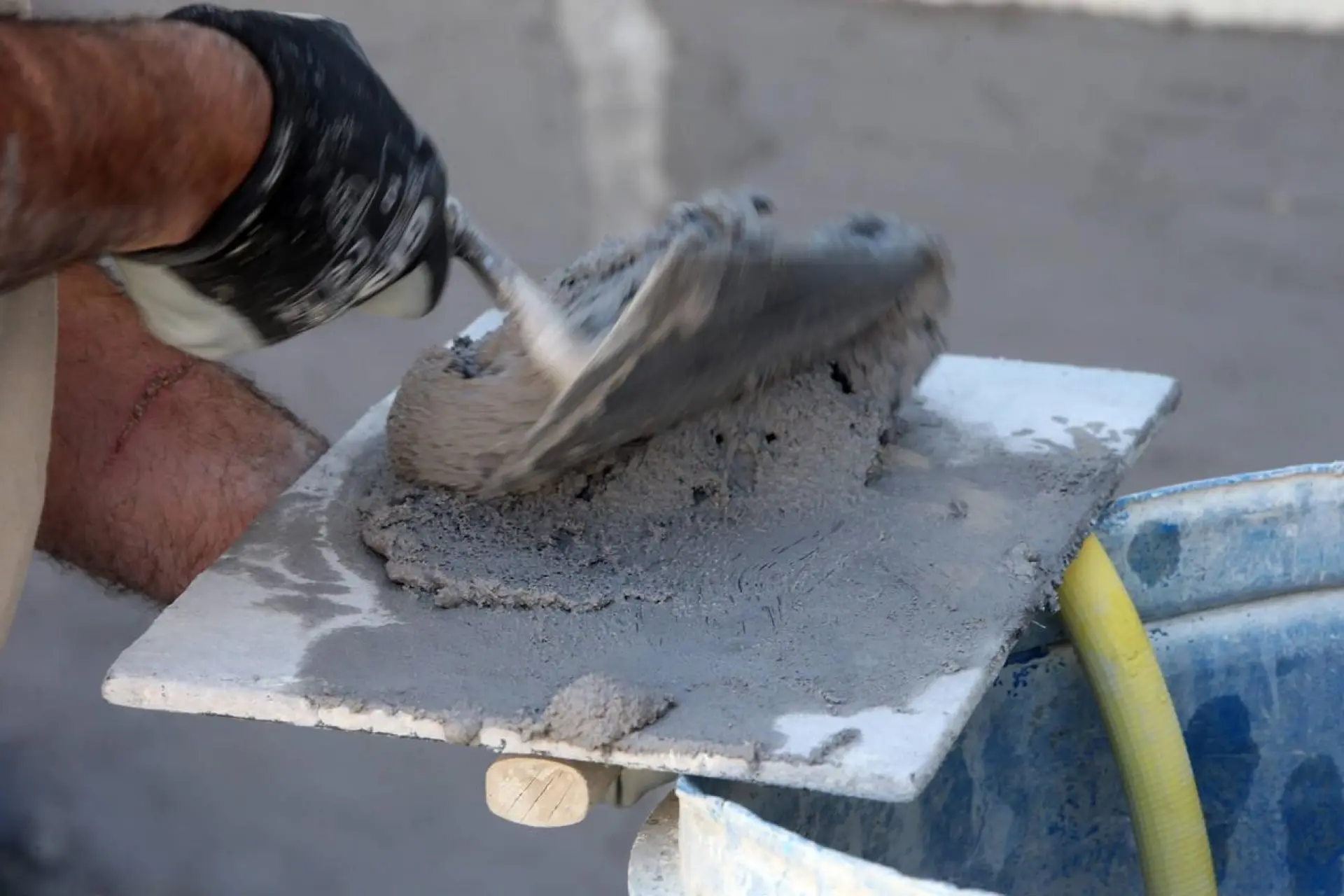 Artisan maçon préparant du ciment sur son lieu de travail, avec un focus sur la truelle et le mortier.