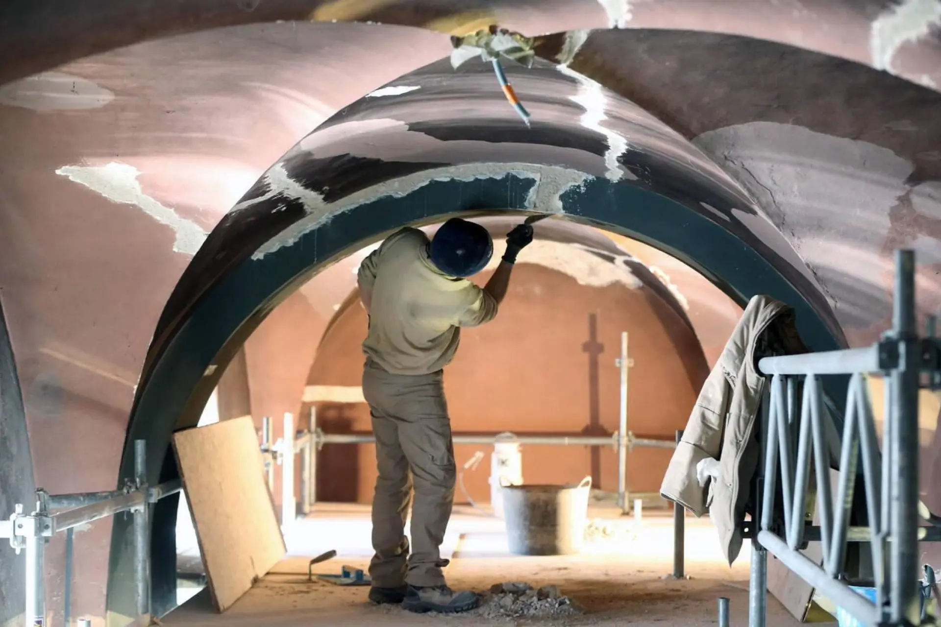 Ouvrier en bâtiment travaillant à l'intérieur d'une structure en arc, appliquant du plâtre ou du stuc sur un plafond voûté.