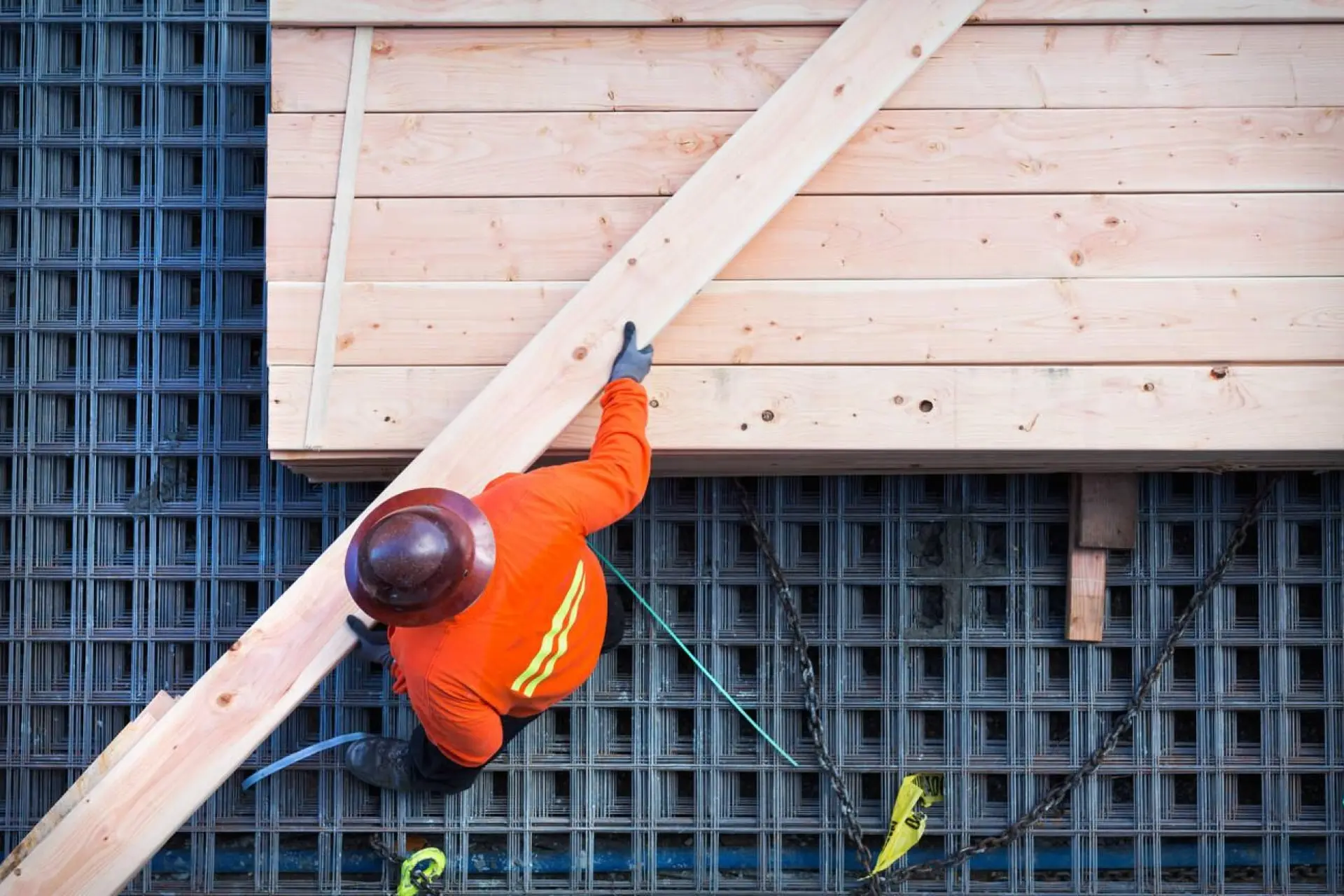 Ouvrier en tenue de sécurité fixant des poutres en bois sur l'armature métallique d'une construction