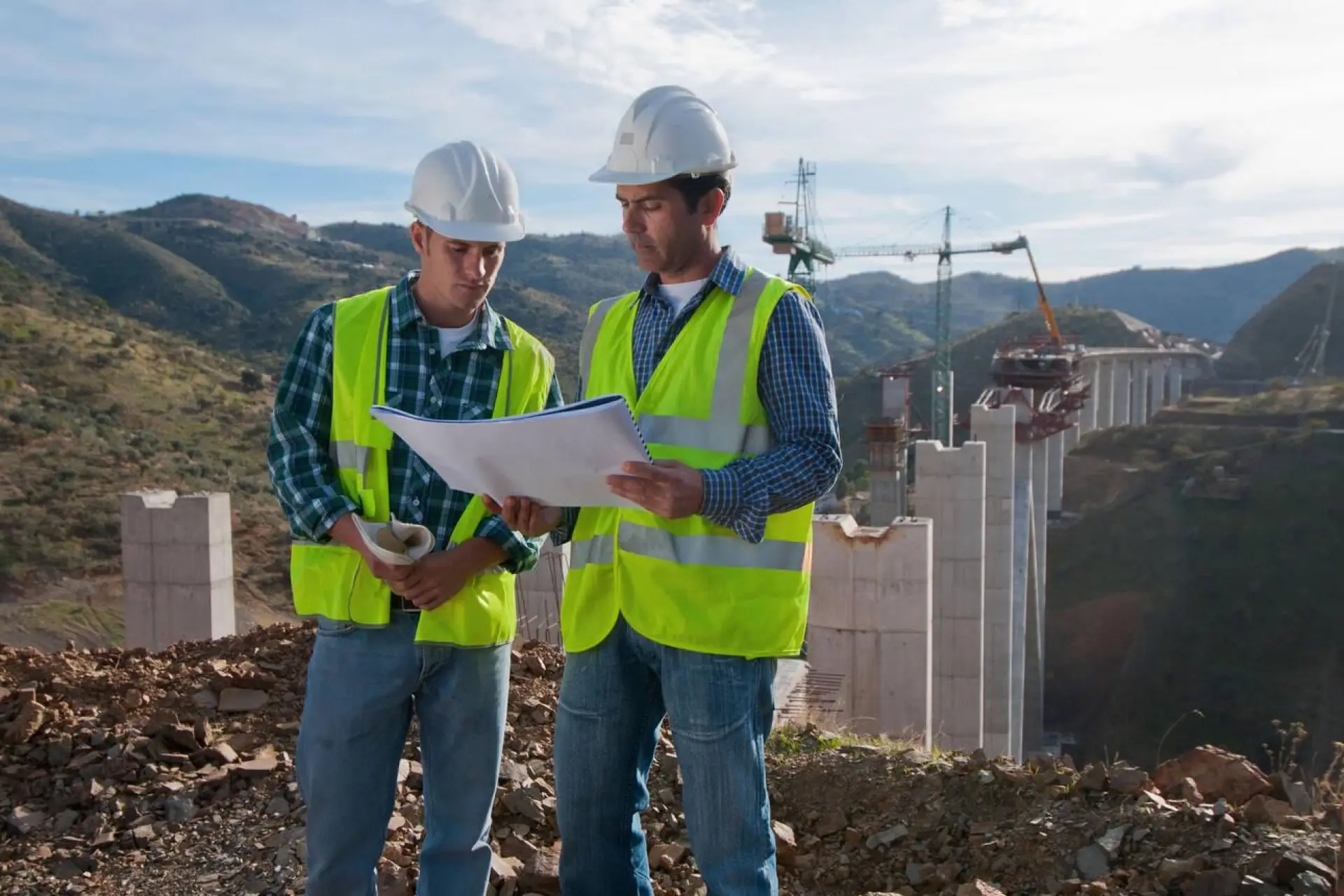 Deux ingénieurs en gilets de sécurité examinant des plans sur un site de construction en plein air