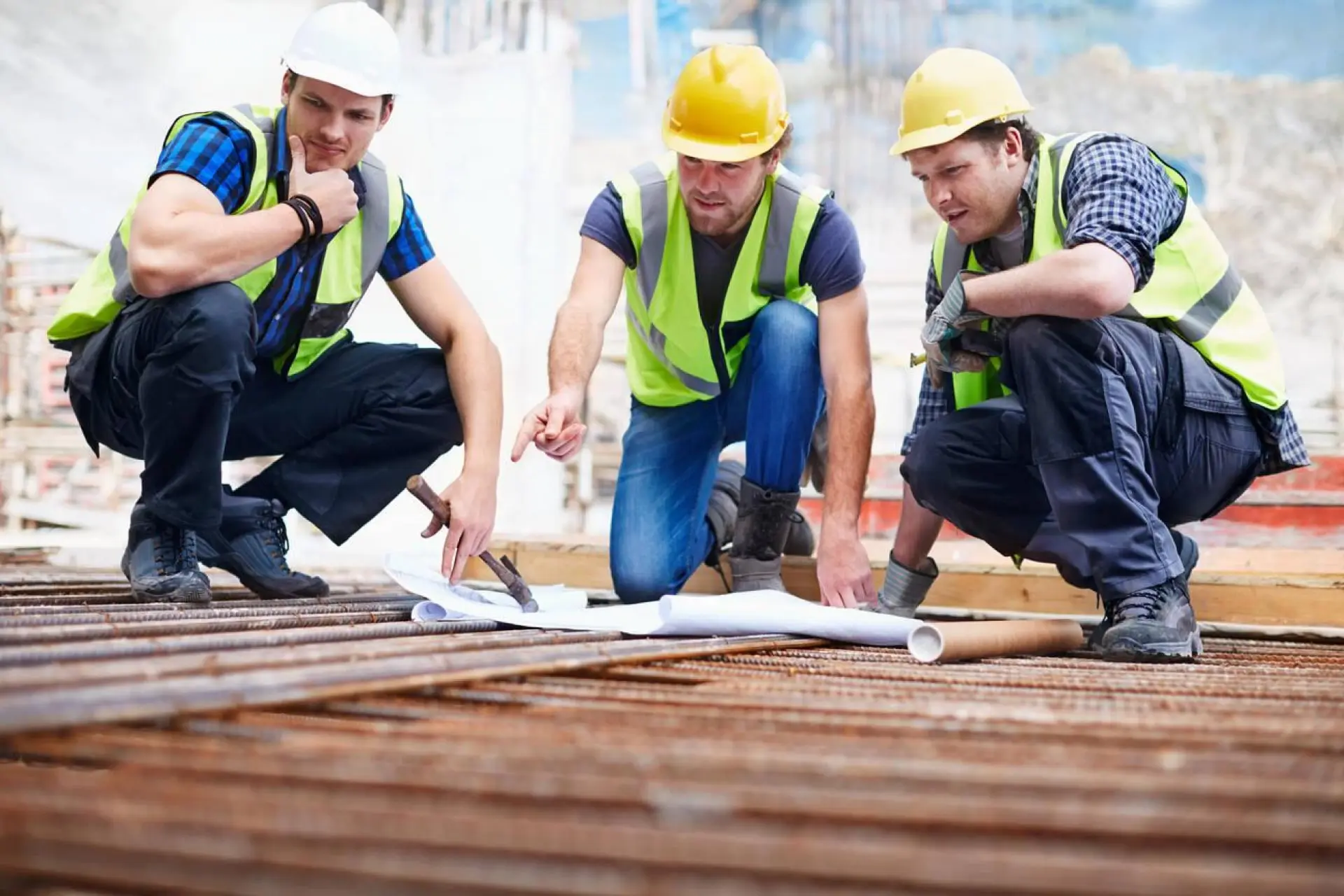 Trois ouvriers en gilet de sécurité analysant des plans sur un chantier de construction