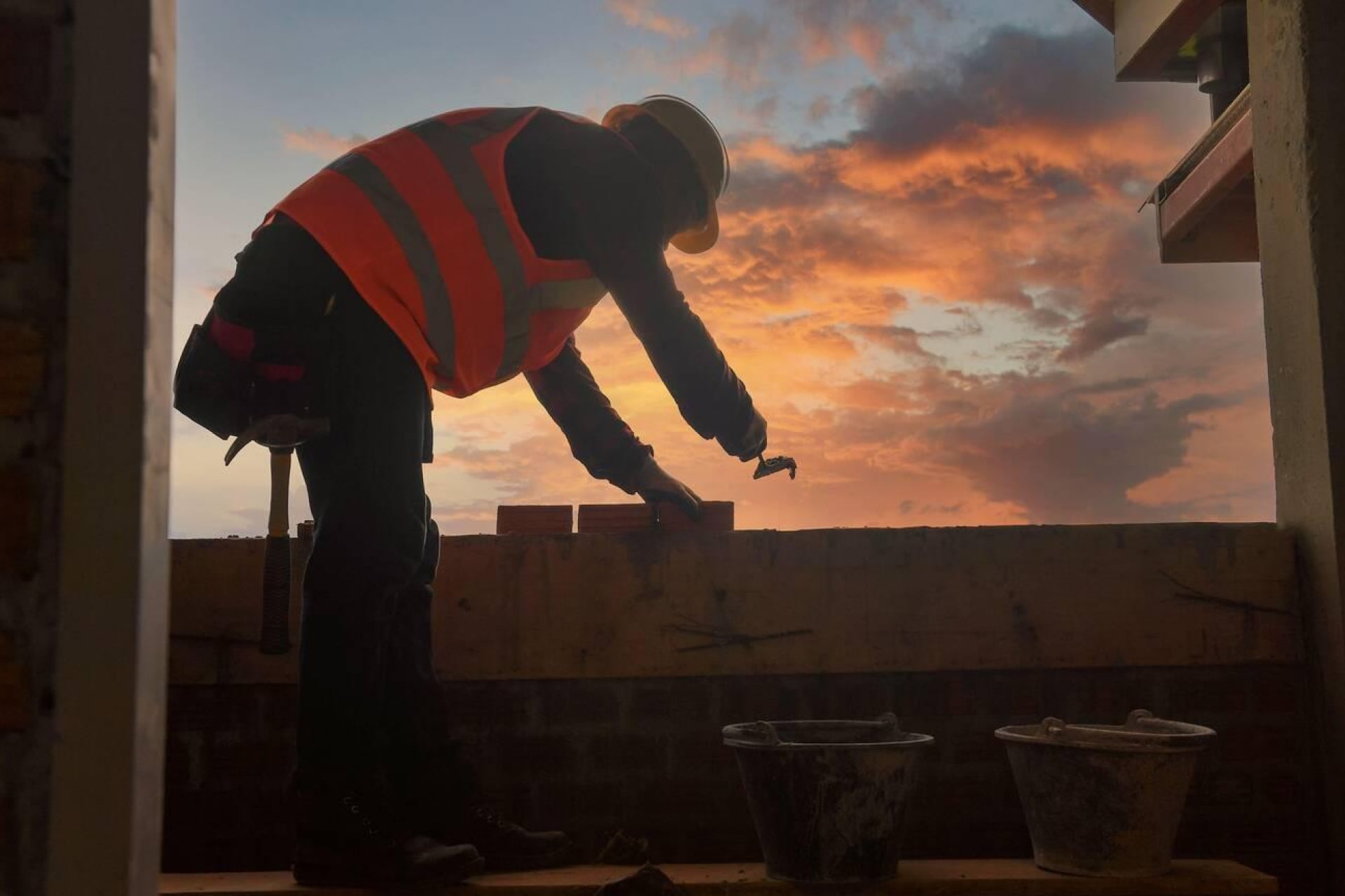 Ouvrier en gilet réfléchissant travaillant sur un mur de briques au crépuscule.