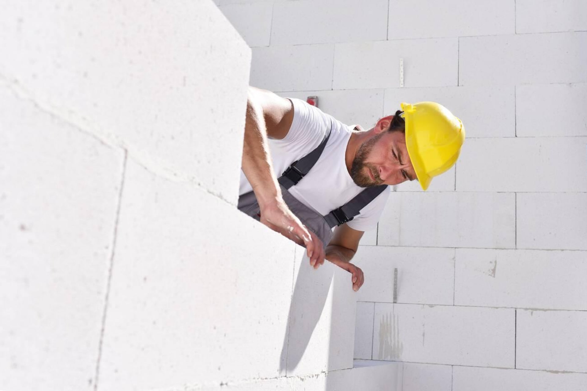 Ouvrier en casque de sécurité examinant un mur de blocs de béton.