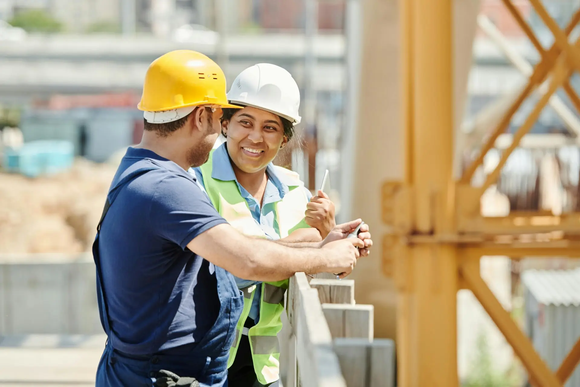 Deux professionnels de la construction, un homme et une femme, discutent et consultent un plan sur une tablette sur un chantier, symbolisant la collaboration et la planification dans le bâtiment.