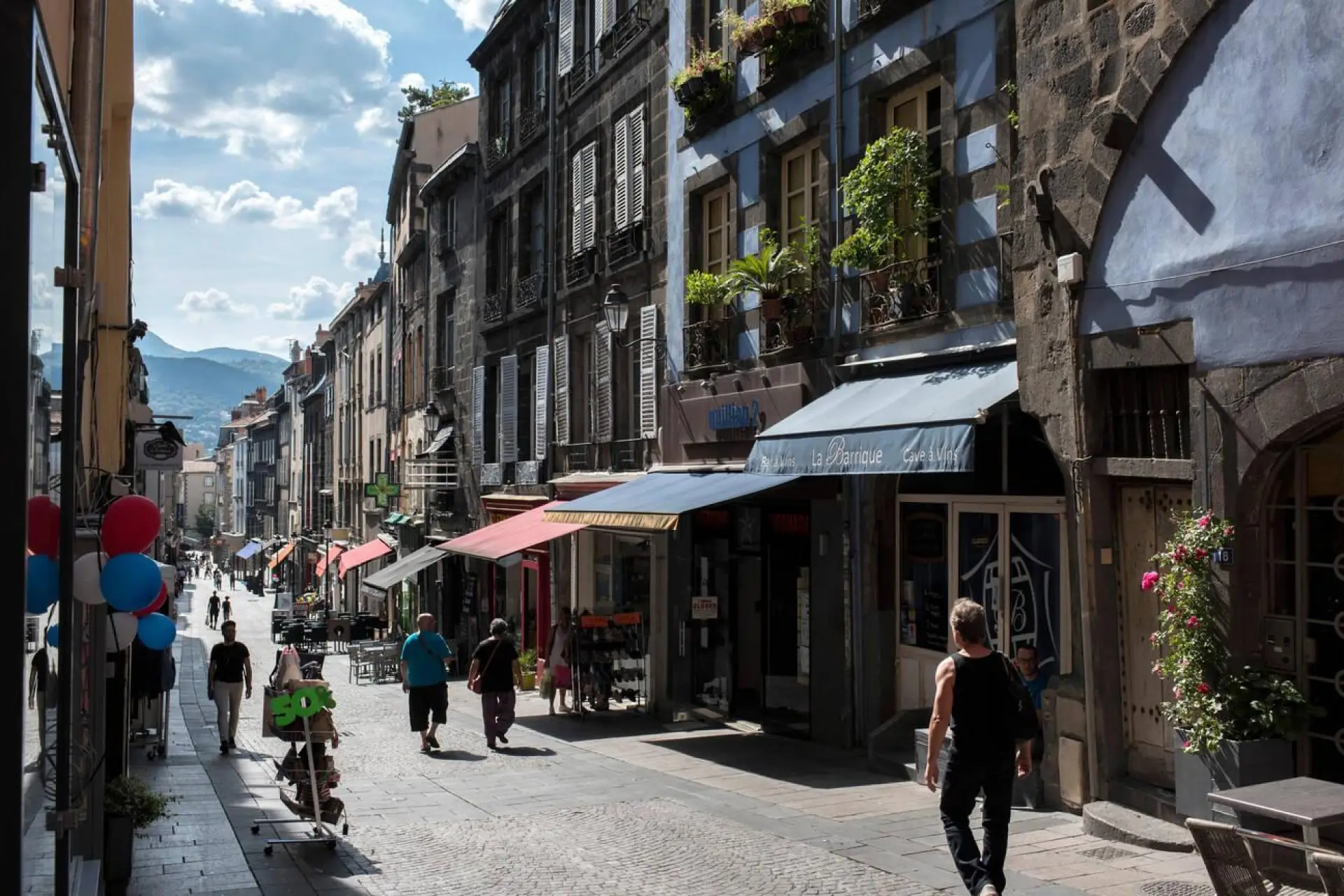 Rue animée de Clermont-Ferrand avec des bâtiments historiques et des passants.