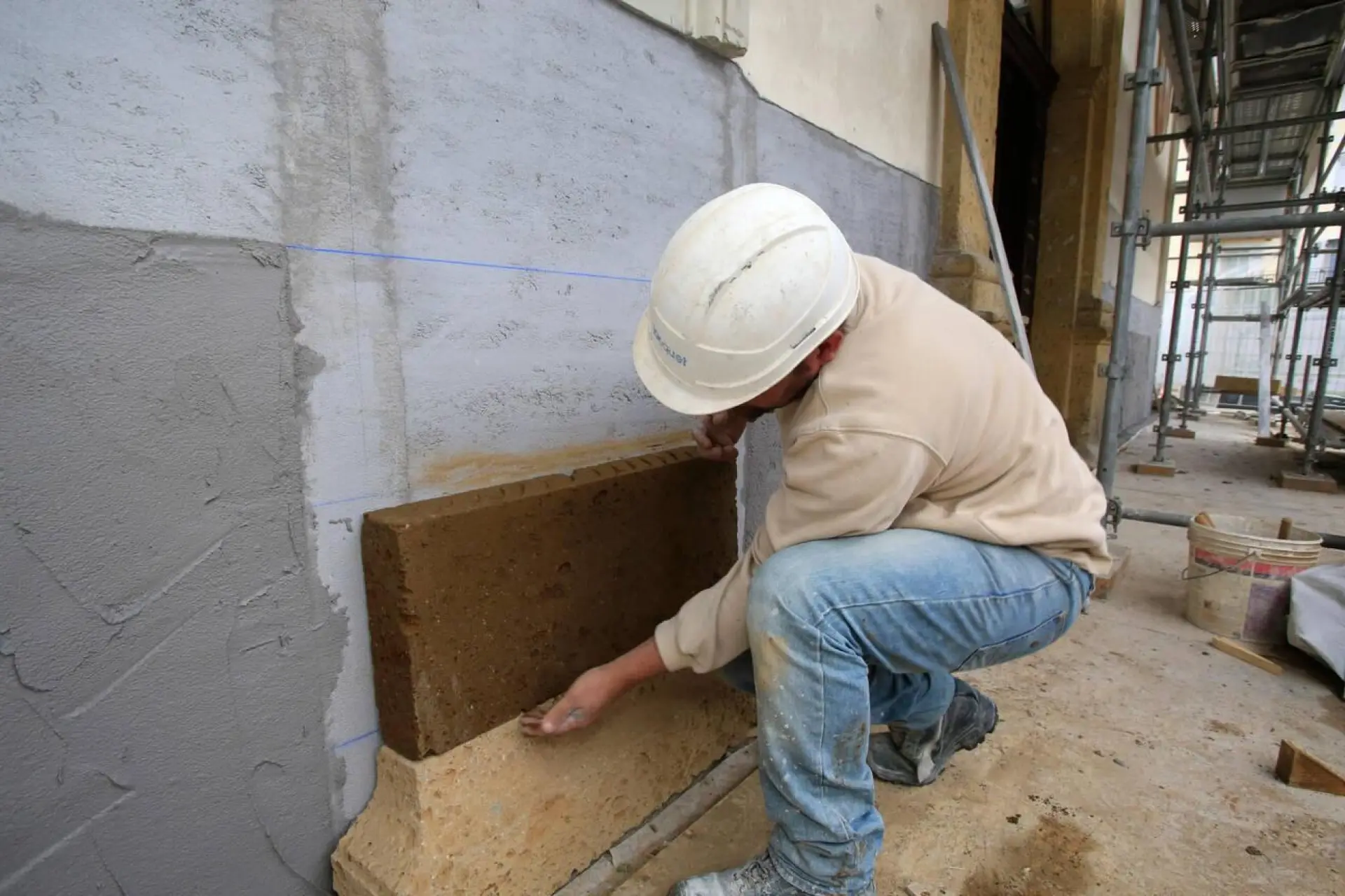 Gros plan sur les mains d'un artisan appliquant du mortier sur un mur en restauration.