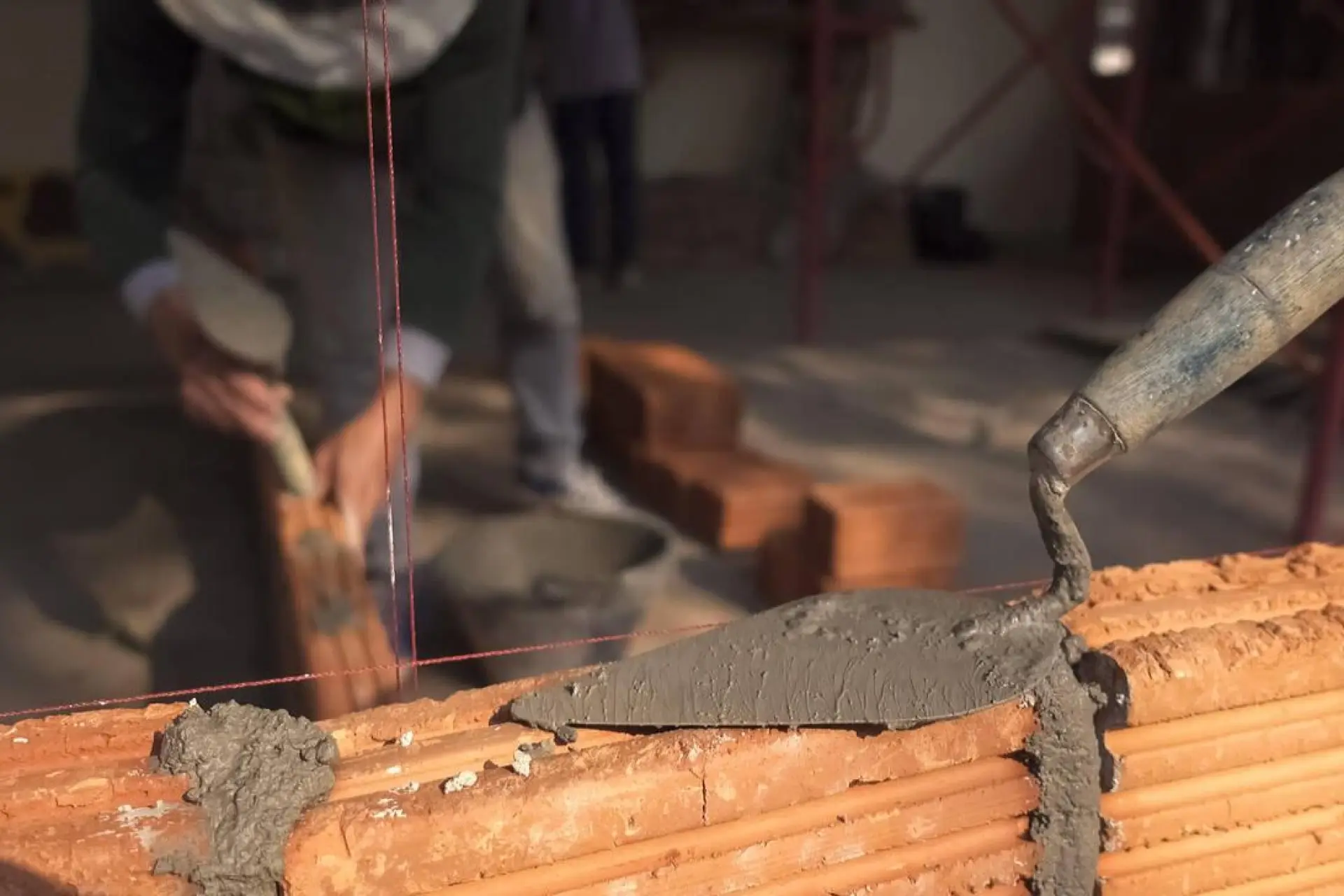 Artisan maçon utilisant une truelle pour appliquer du mortier entre les briques, soulignant le soin et l'attention aux détails.